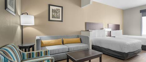 A hotel room with a bed, a sofa, a coffee table, a lamp, and framed pictures on the wall.