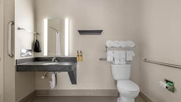 Un baño con lavamanos, espejo, inodoro, barras de apoyo y toallas.
