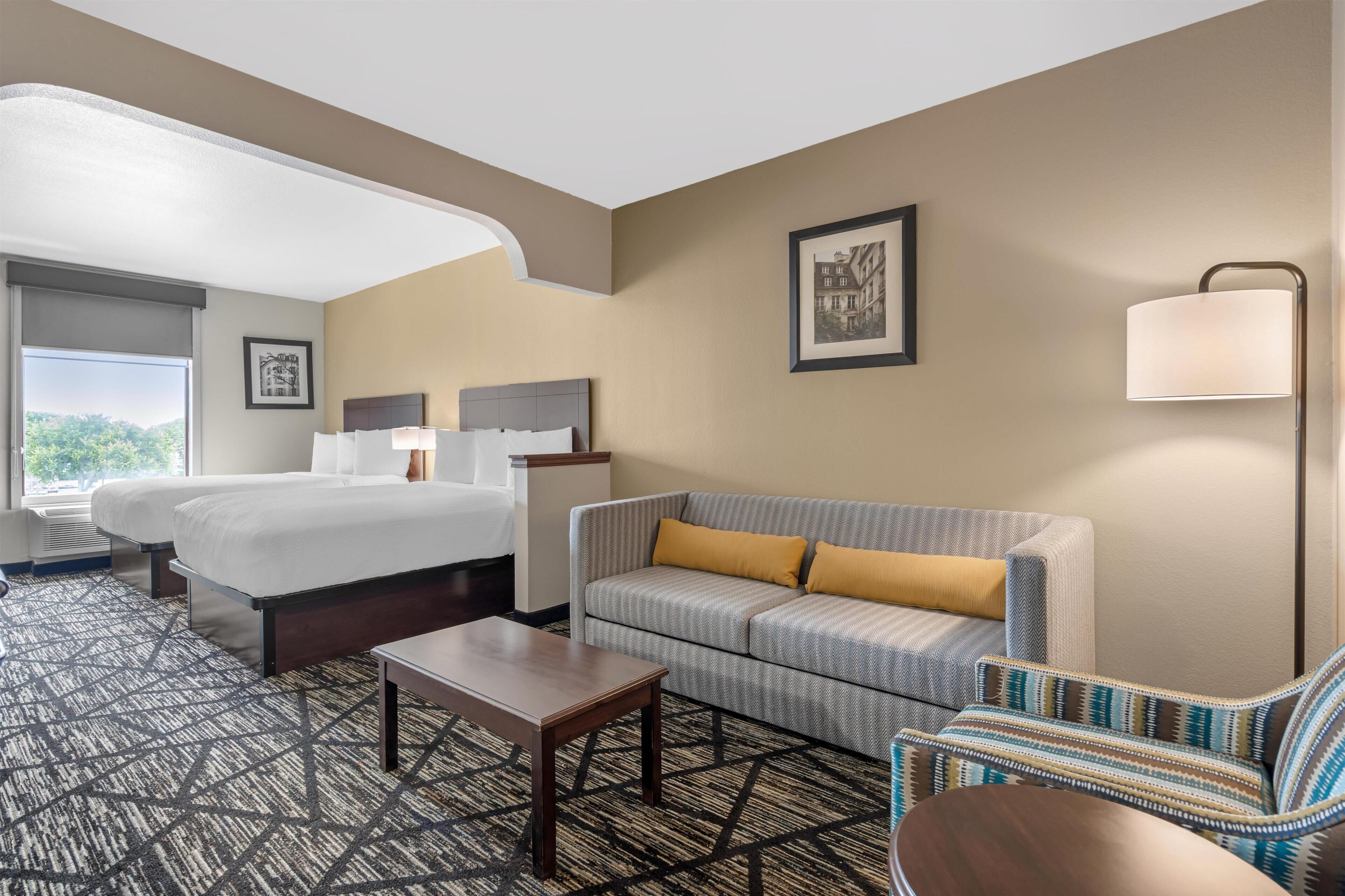 A hotel room with a bed, two bedside tables, a sofa, a chair, a small table, and a lamp.
