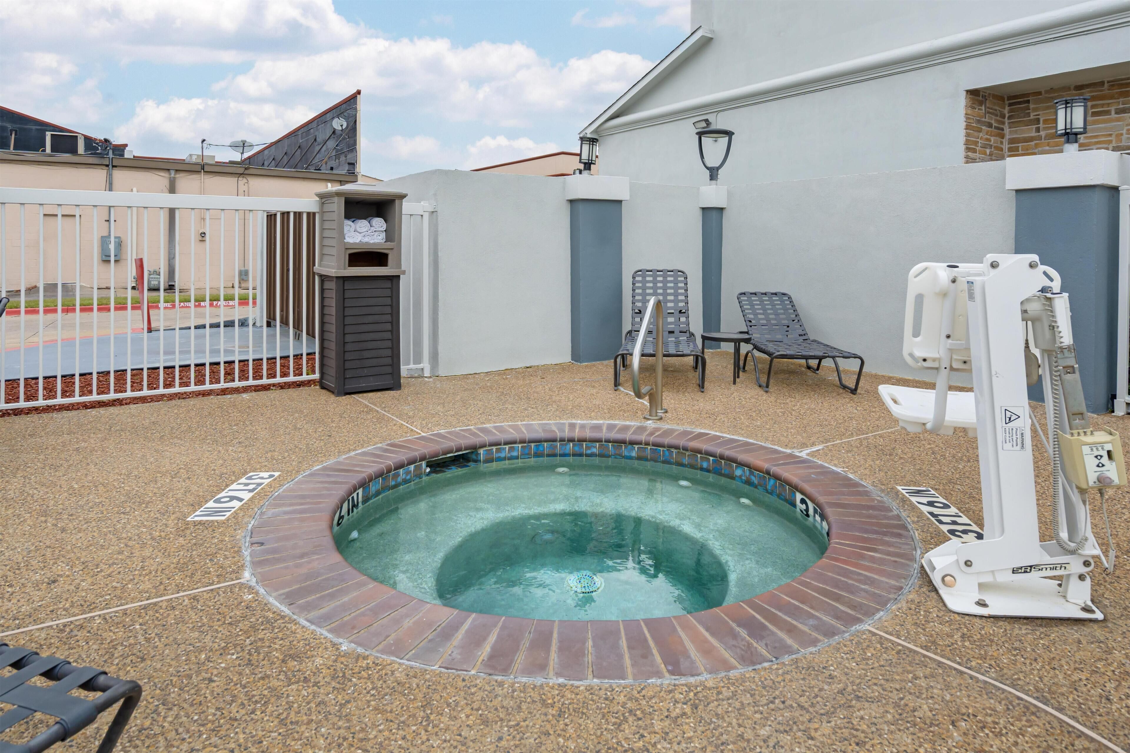 A hot tub surrounded by a white fence, with two lounge chairs and a pool table nearby.