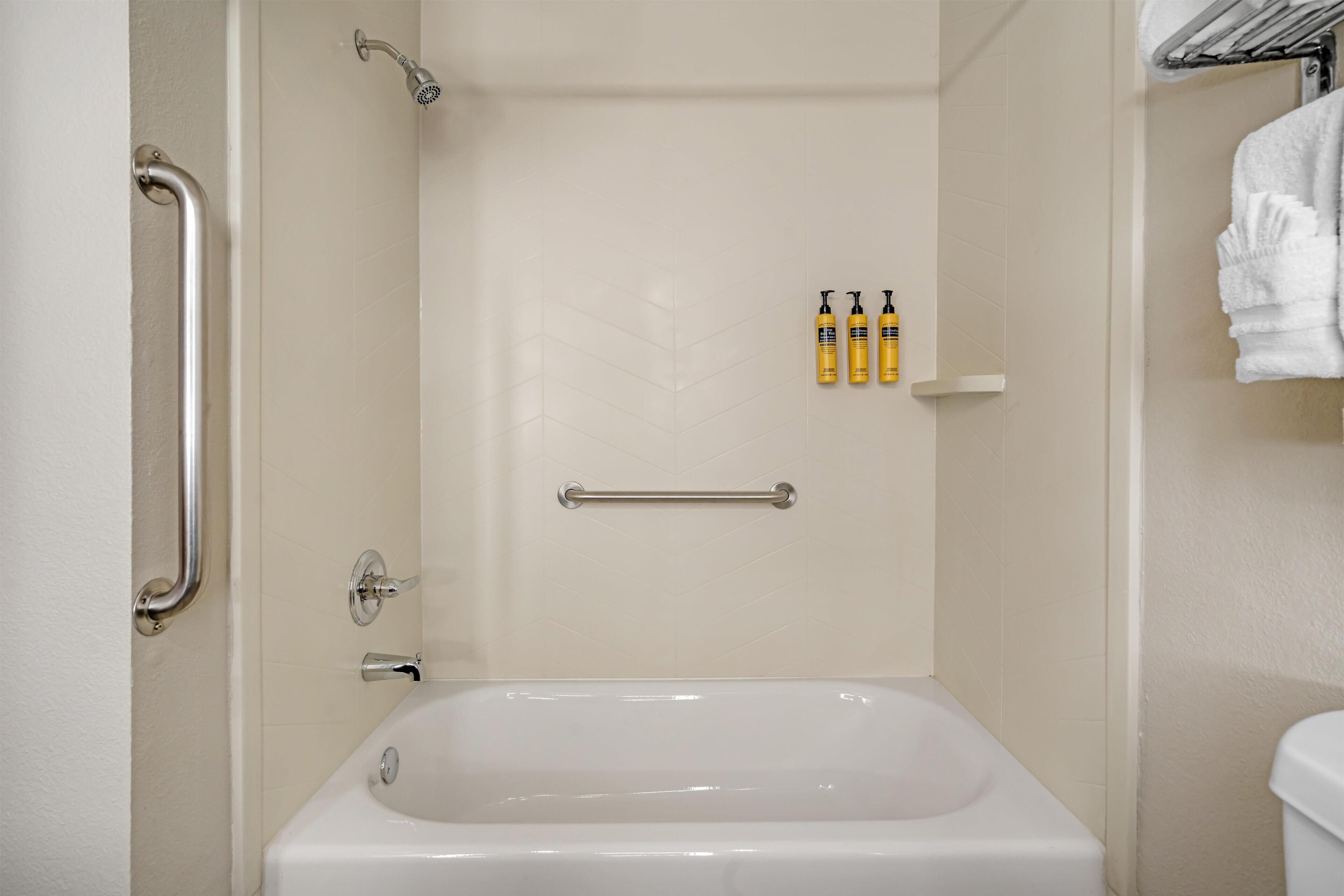 Ein Badezimmer mit einer Badewanne, einer Dusche, einer Haltestange und einem Ablagefach für Toilettenartikel.