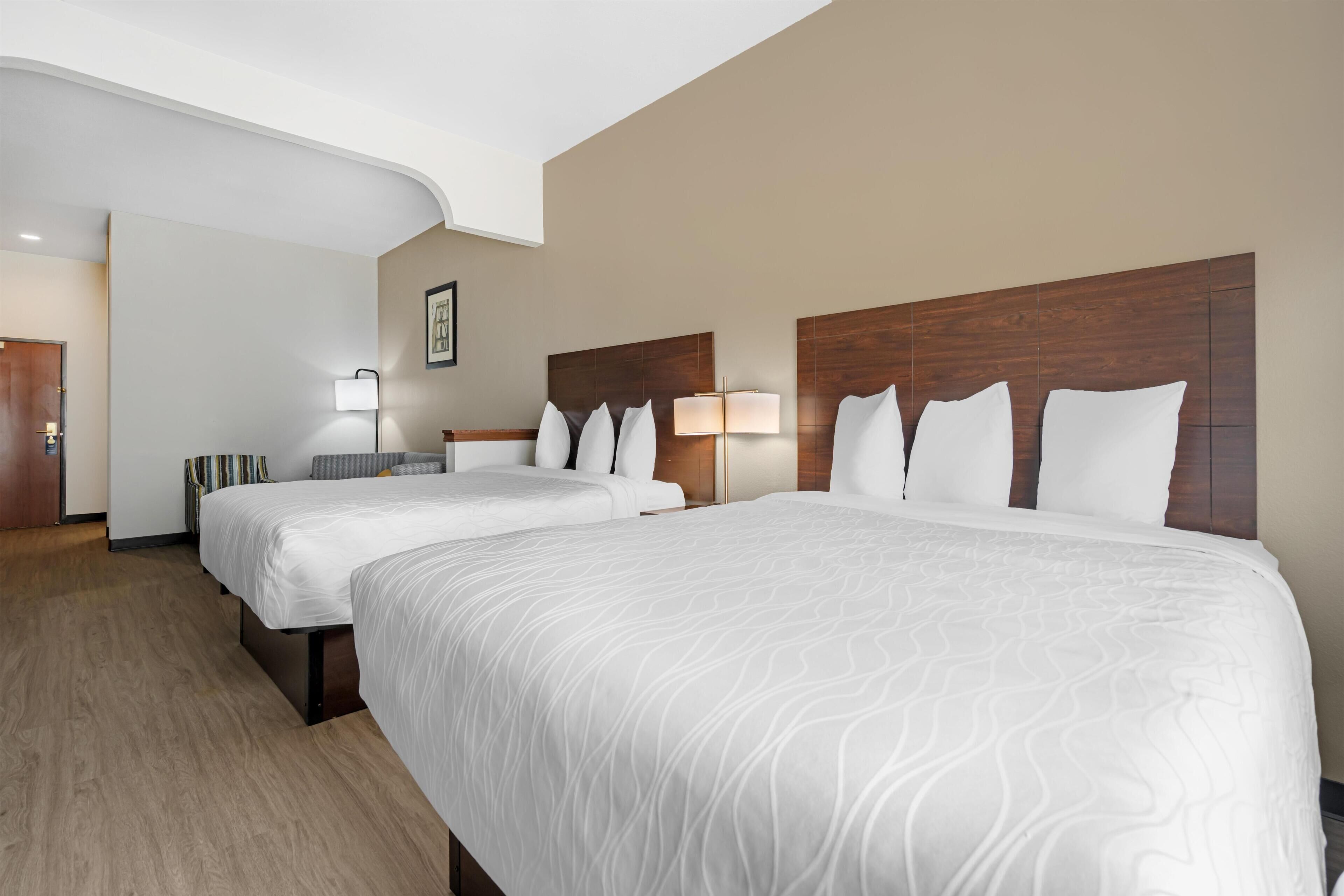 Ein Hotelzimmer mit zwei Betten, einem Holzkopfteil, einer Wandlampe und einem gerahmten Bild.