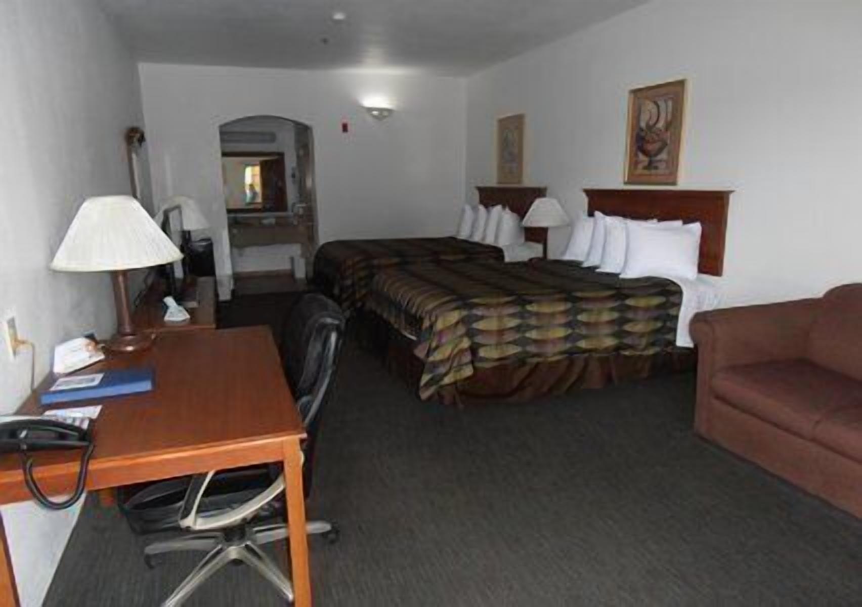 Una camera d'albergo con un letto, una scrivania con una sedia, un divano e una lampada.