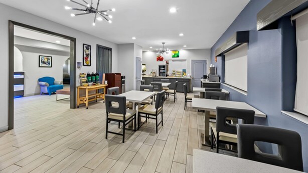 A modern dining area with tables and chairs, a kitchen in the background, and a blue accent wall. - Quality Inn & Suites Rio Grande City (Rio Grande City)