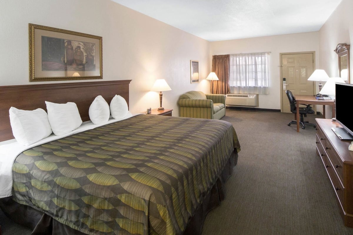 Une chambre d’hôtel avec un grand lit, un bureau, une chaise, une télévision et une fenêtre avec des rideaux.