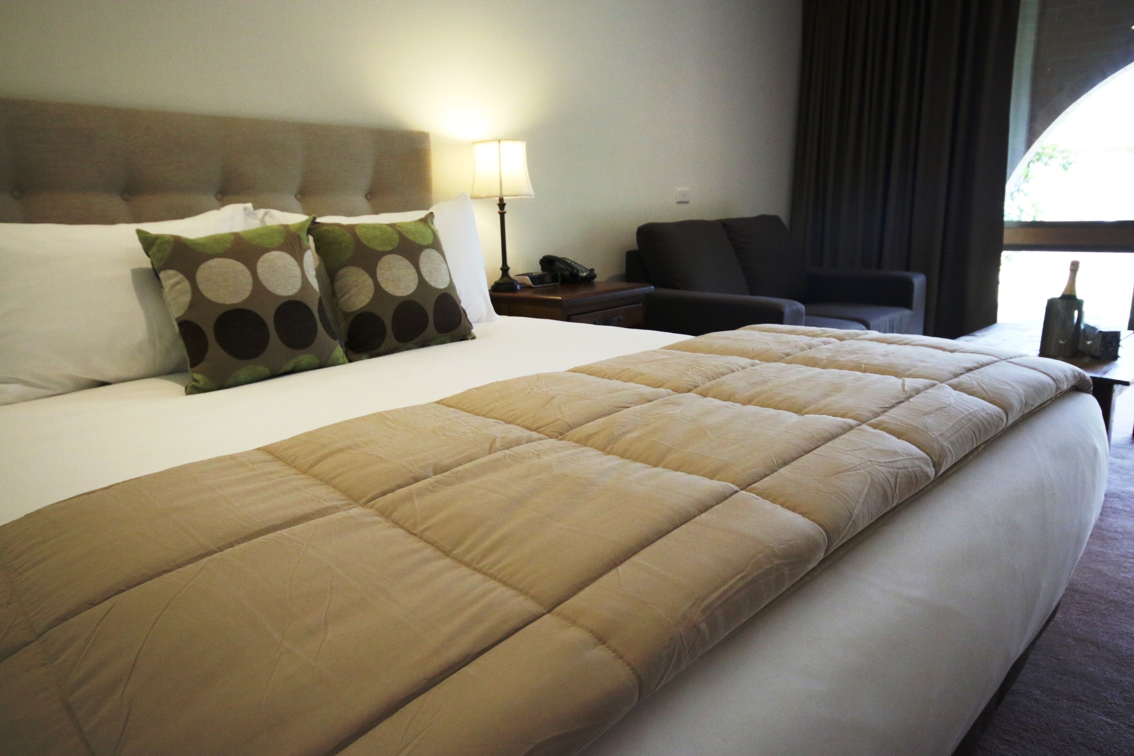 A hotel room with a large bed, a nightstand with a lamp, a chair, and a window with curtains.