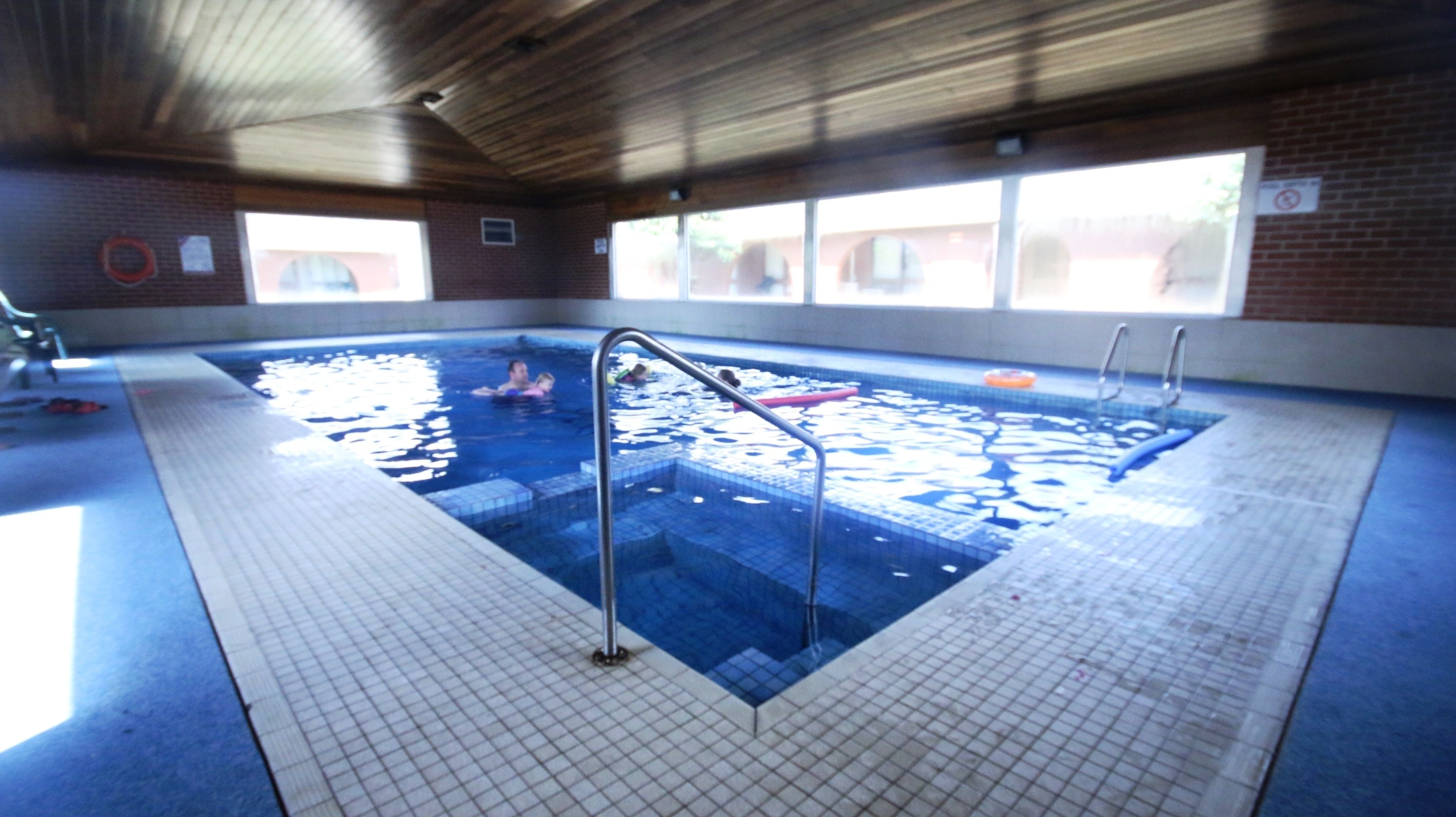 Una piscina interior con agua cristalina, suelo de baldosas y escaleras metálicas.