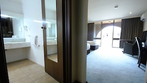 A hotel room with a bathroom, a large mirror, a bed, a desk, and a view of the outside. - Bell Tower Inn (Alfredton)