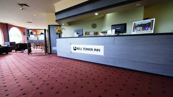 A reception desk at the Bell Tower Inn with a clock, a computer monitor, and a vase with flowers.