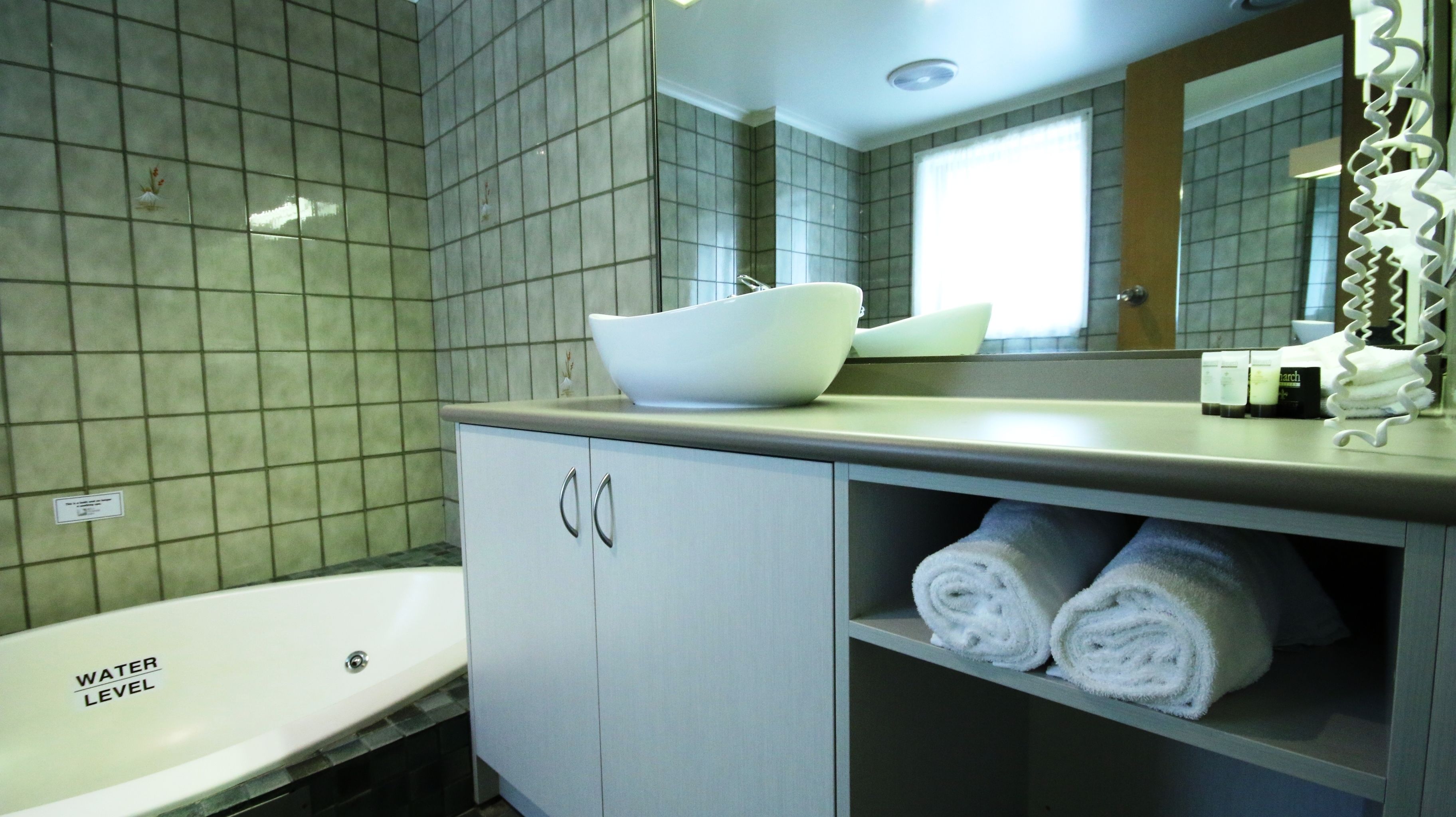 Un baño moderno con un lavamanos blanco, una bañera y un espejo sobre el lavamanos.