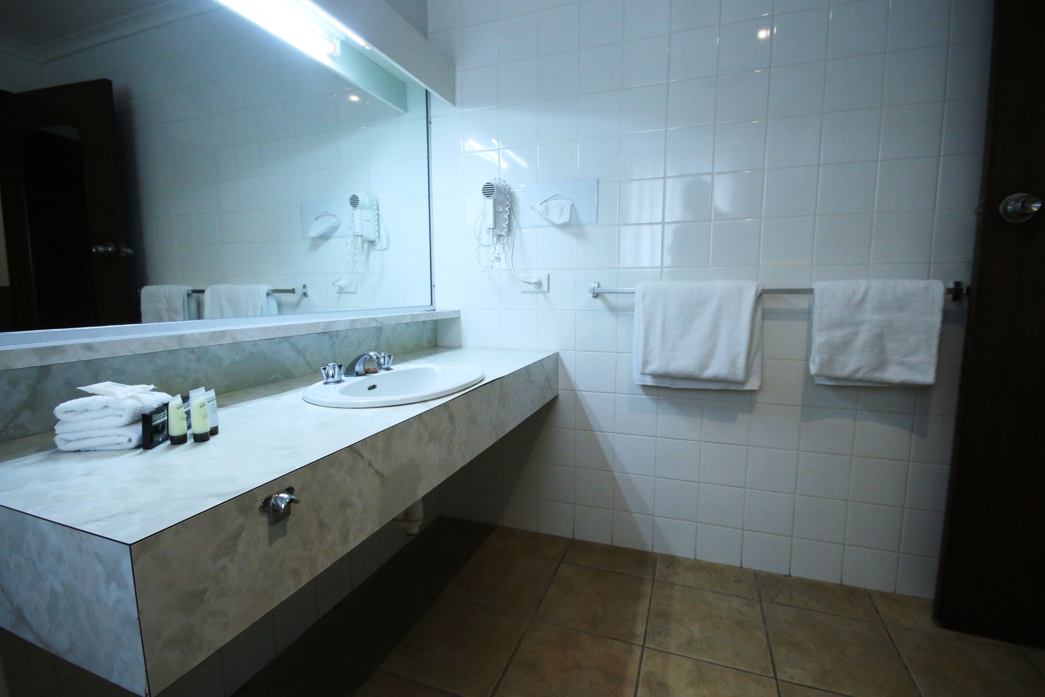 A bathroom with a marble vanity, a sink, a mirror, and white tiled walls.
