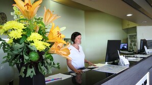 A reception desk with a vase of yellow flowers and a woman standing behind it. - Bell Tower Inn (Alfredton)