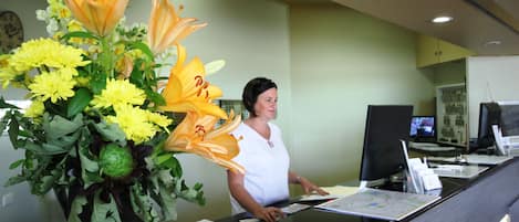 Mostrador de recepción con un jarrón de flores amarillas y una mujer detrás.