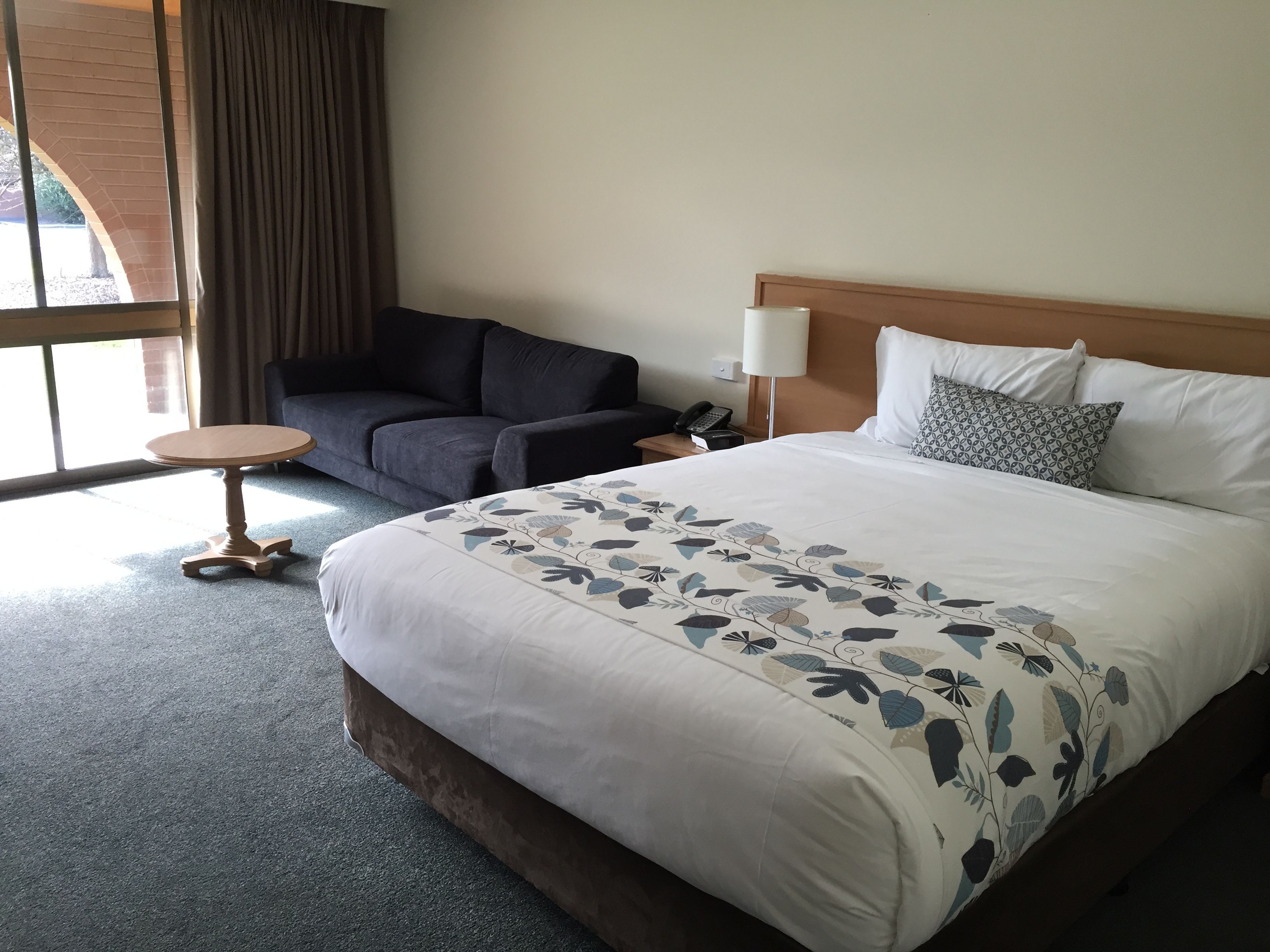 A hotel room with a large bed, a small round table, a sofa, and a lamp.