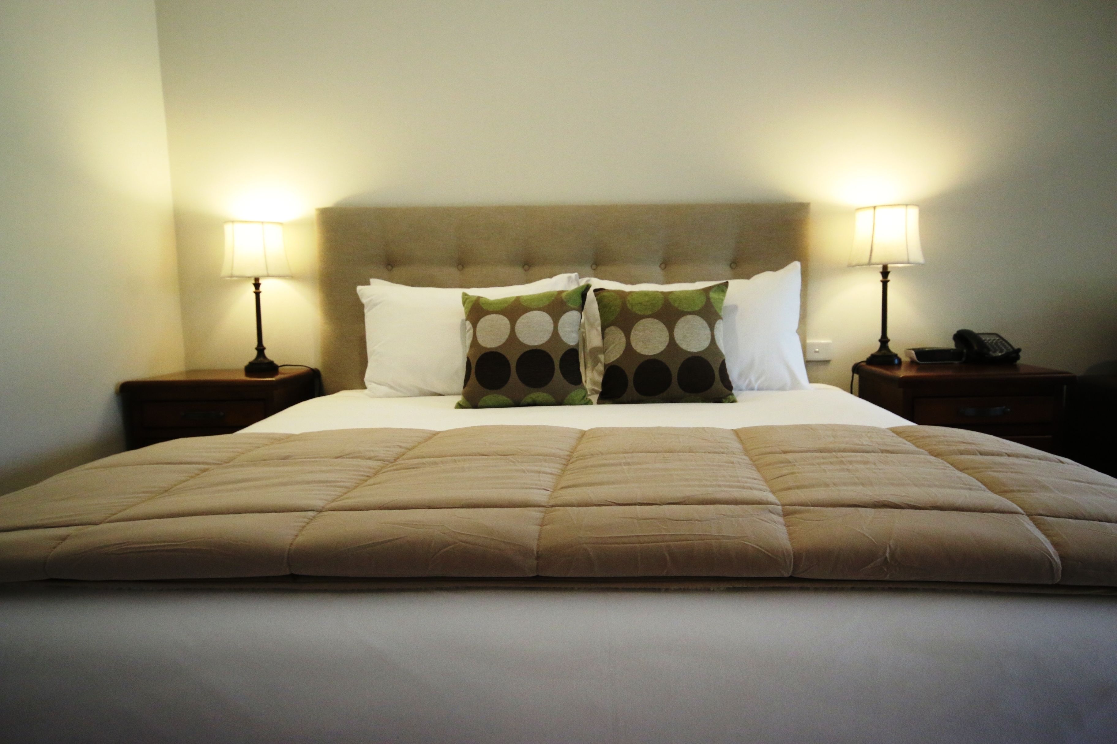 A neatly made bed with a beige duvet, two pillows with a circular pattern, and two bedside lamps on wooden nightstands.