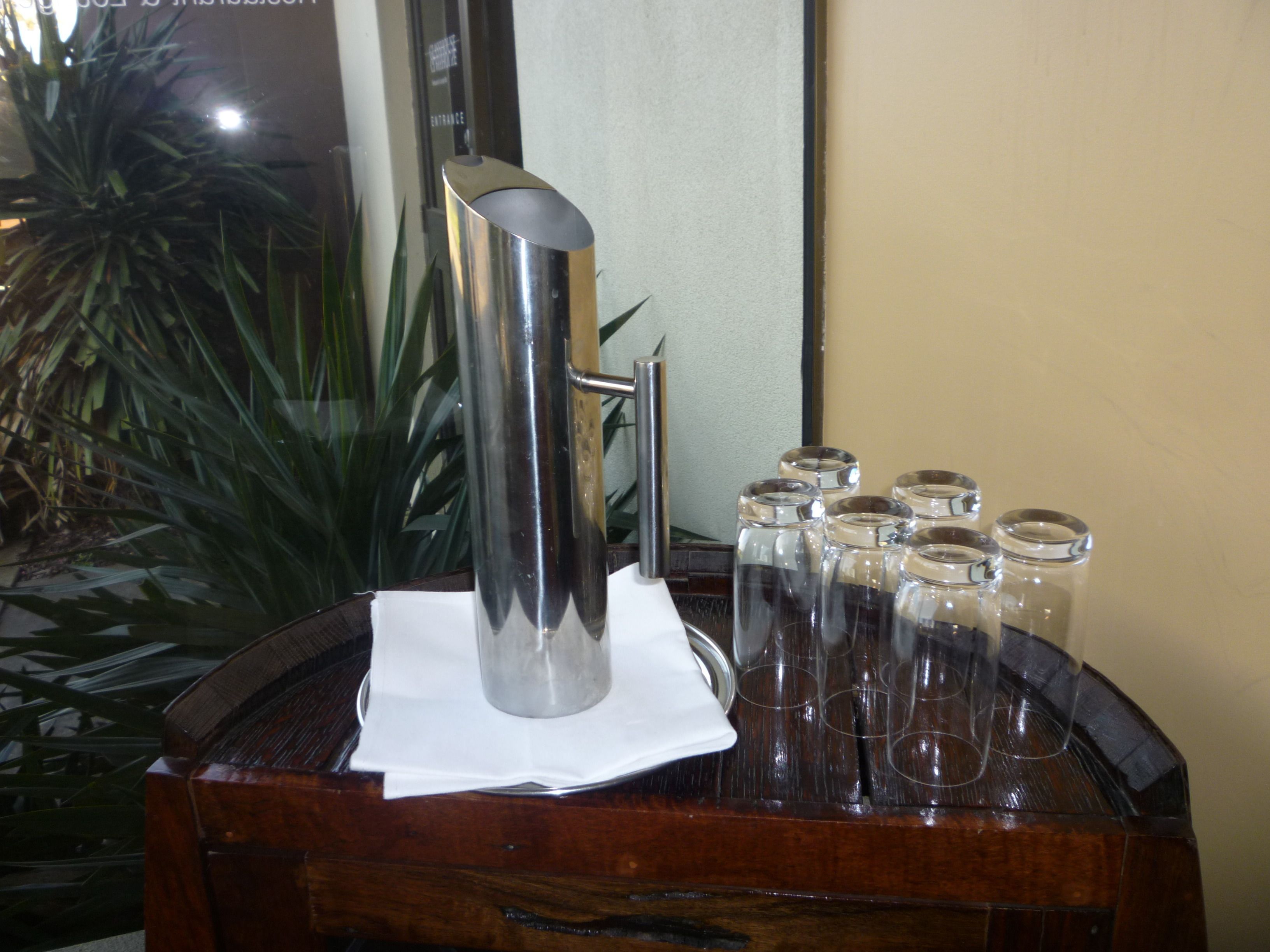 A metallic pitcher on a wooden table with a white napkin, surrounded by clear glass jars.