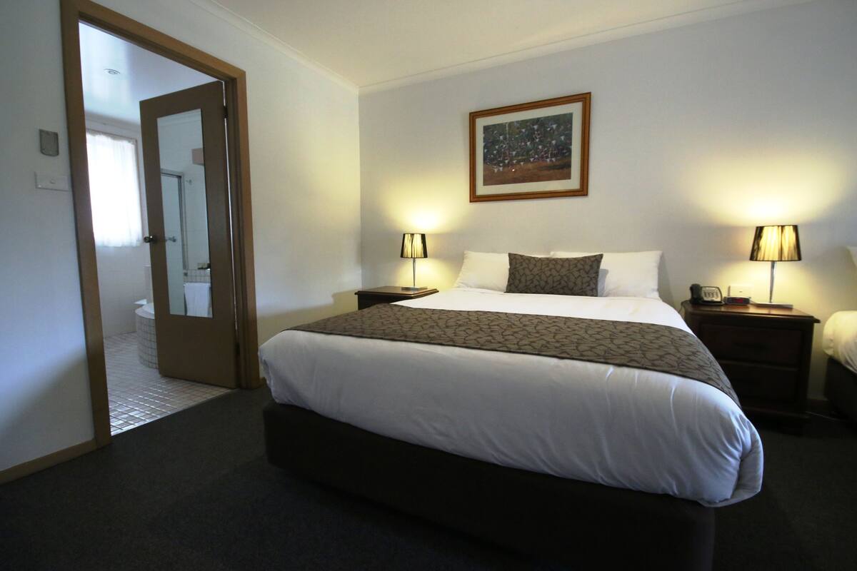 A hotel room with a large bed, two bedside tables with lamps, a framed picture on the wall, and a door leading to a bathroom.