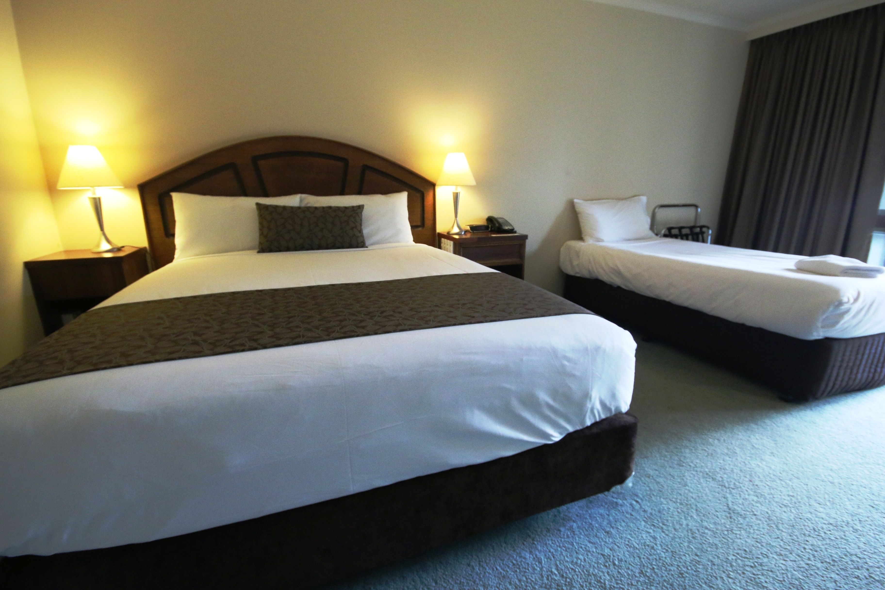 Una habitación de hotel con dos camas individuales, cada una con una almohada, una mesita de noche con lámpara y teléfono.