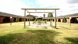 A courtyard with a pergola, a central table, and chairs. There are brick buildings with arched windows in the background. - Bell Tower Inn (Alfredton)