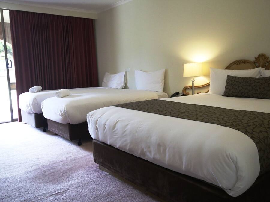A hotel room with two beds, a large window with curtains, and a nightstand with a lamp.