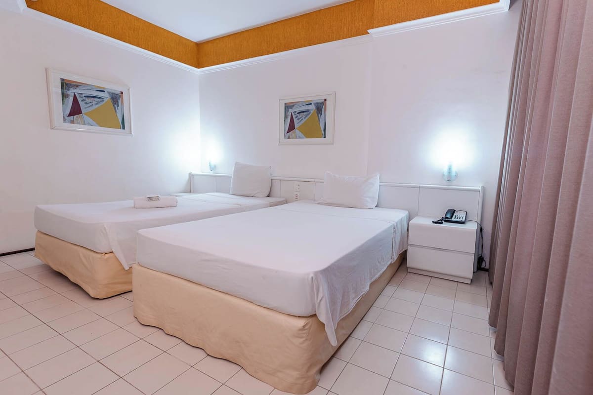 A hotel room with two beds, a bedside table with a phone, and artwork on the walls.