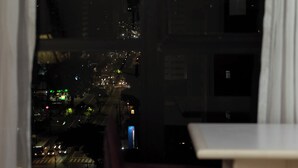 A nighttime city view from a window with a table and chair in the foreground. - Rede Andrade LG Inn (Recife)