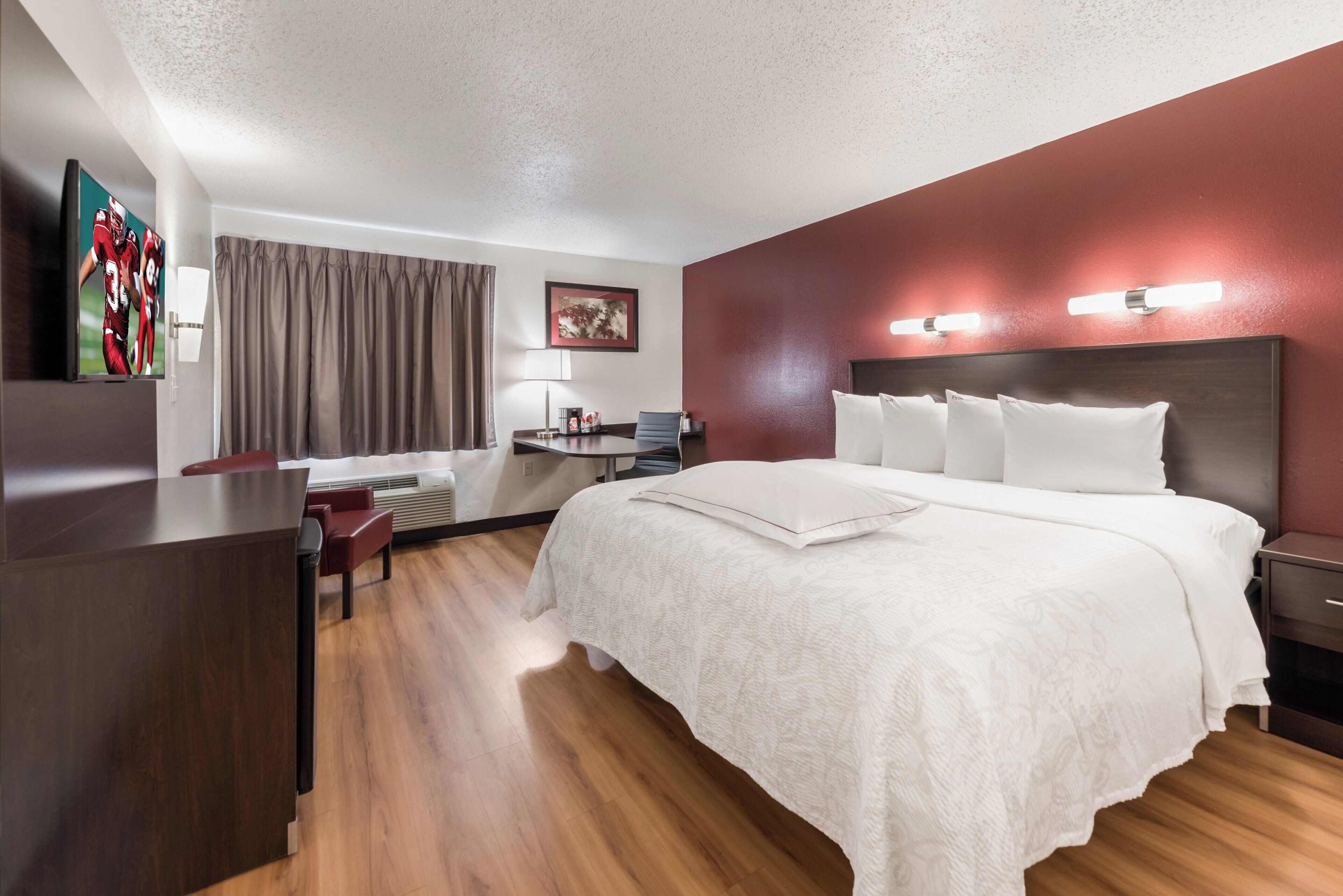 A hotel room with a large bed, a desk, a chair, a flat-screen TV, and a window with curtains.