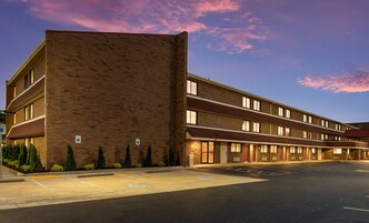 A multi-story hotel with a brick facade, a parking lot, and a clear sky.