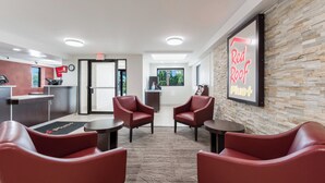 A reception area with a desk, chairs, a clock, and a wall-mounted sign. - Red Roof Inn PLUS+ Columbus - Worthington (Columbus)