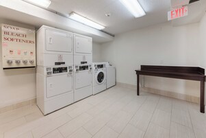 A laundry room with stacked washers and dryers, an exit sign, and a coin-operated soap dispenser.