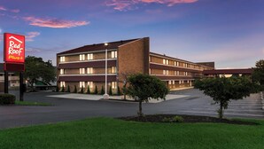 A multi-story hotel with a flat roof, a parking lot, and a sign for Red Roof Plus. - Red Roof Inn PLUS+ Columbus - Worthington (Columbus)