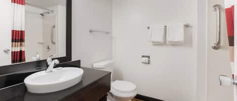 A modern bathroom with a white sink, a mirror, a toilet, and a shower area.