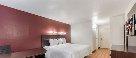 A hotel room with a bed, a desk, a chair, and a door.