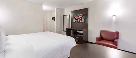 Ein Hotelzimmer mit einem Bett, einem Schreibtisch, einem Sessel und einem an der Wand befestigten Fernseher.