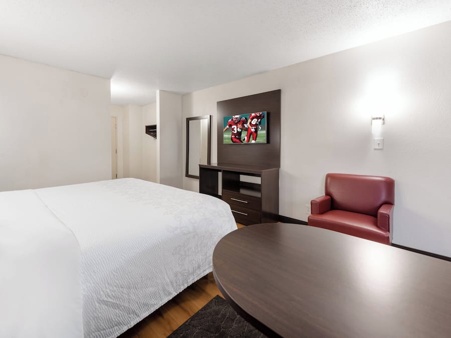 A hotel room with a bed, a desk, a chair, and a TV mounted on the wall.