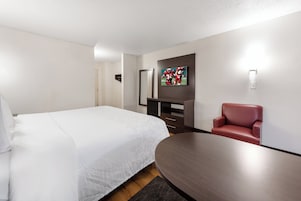 A hotel room with a bed, a desk, a chair, and a TV mounted on the wall.