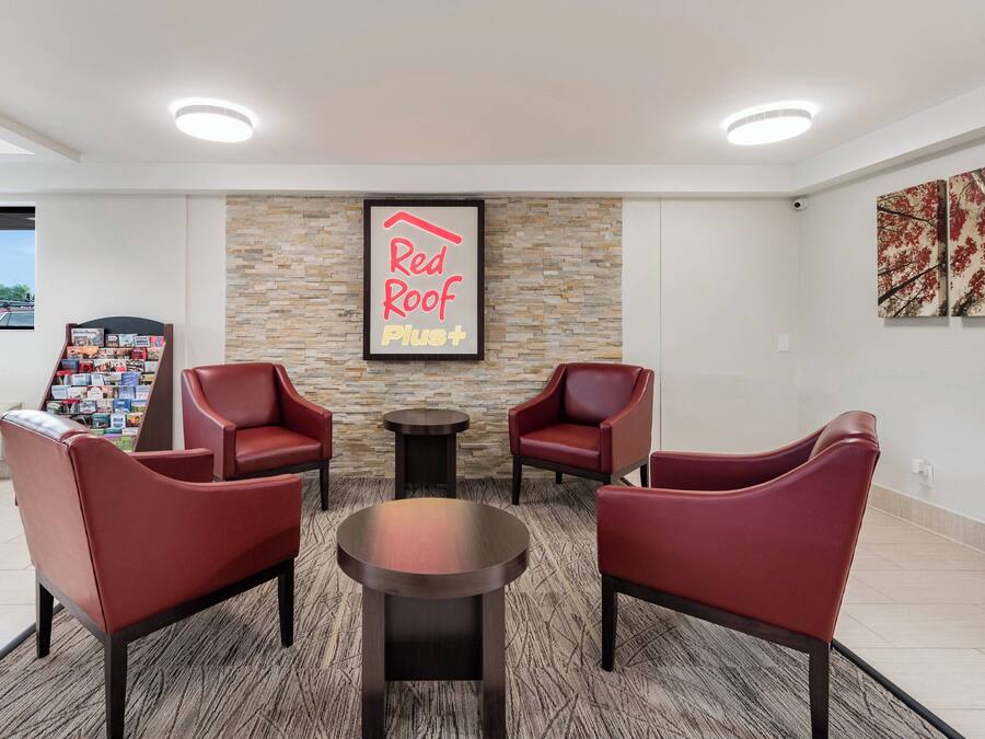A Red Roof Plust lounge area with two red chairs, a small table, and a stone wall.