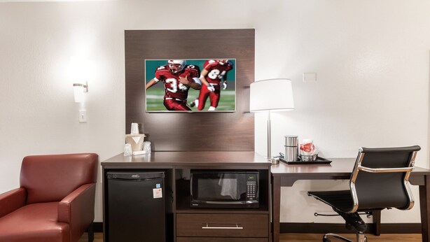 A hotel room with a desk, a microwave, a refrigerator, a red leather chair, a black office chair, a flat-screen TV, and a lamp. - Red Roof Inn PLUS+ Columbus - Worthington (Columbus)