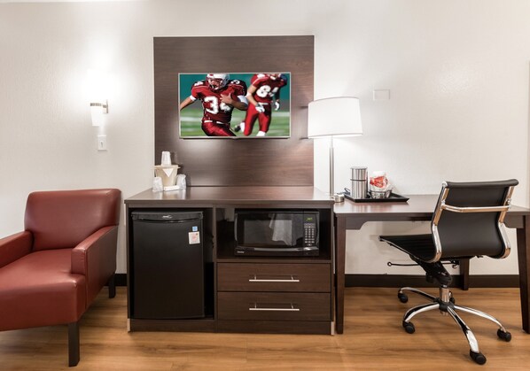 A hotel room with a desk, a microwave, a refrigerator, a red leather chair, a black office chair, a flat-screen TV, and a lamp. - Red Roof Inn PLUS+ Columbus - Worthington (Columbus)