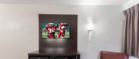 A living room with a flat-screen TV mounted on a wooden cabinet, a microwave, and a red leather chair.