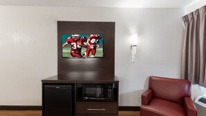 A compact living space with a flat-screen TV mounted on a dark cabinet, a microwave, and a red leather chair. - Red Roof Inn PLUS+ Columbus - Worthington (Columbus)