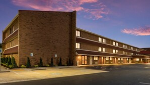 A multi-story hotel with a brick facade, a parking lot, and a clear sky with pink clouds. - Red Roof Inn PLUS+ Columbus - Worthington (Columbus)