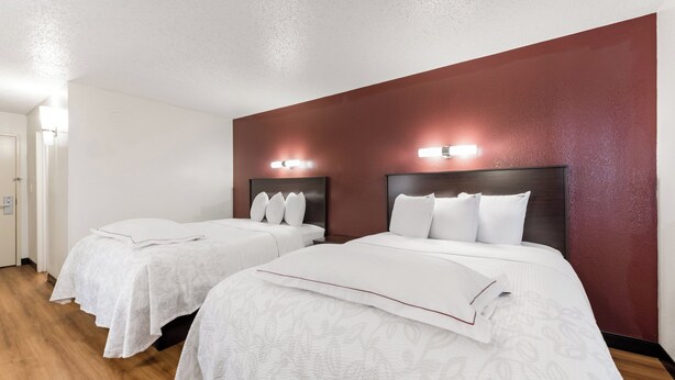 A hotel room with two beds, a wooden floor, and a red accent wall. - Red Roof Inn PLUS+ Columbus - Worthington (Columbus)