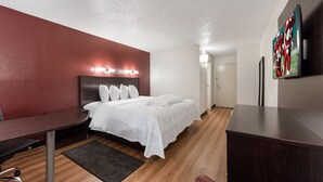 A modern hotel room with a neatly made bed, a desk with a chair, and a flat-screen TV mounted on the wall. - Red Roof Inn PLUS+ Columbus - Worthington (Columbus)