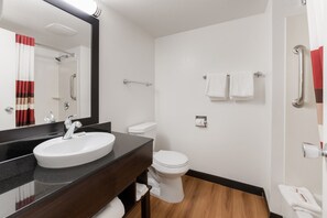A modern bathroom with a white sink, dark countertop, and a mirror above it. There is a toilet with a white tank and a towel rack above it. - Red Roof Inn PLUS+ Columbus - Worthington (Columbus)