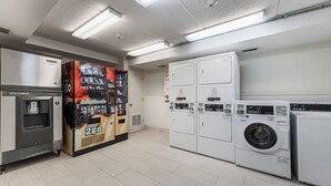 A laundry facility with a vending machine, a refrigerator, and stacked washing machines. - Red Roof Inn PLUS+ Columbus - Worthington (Columbus)