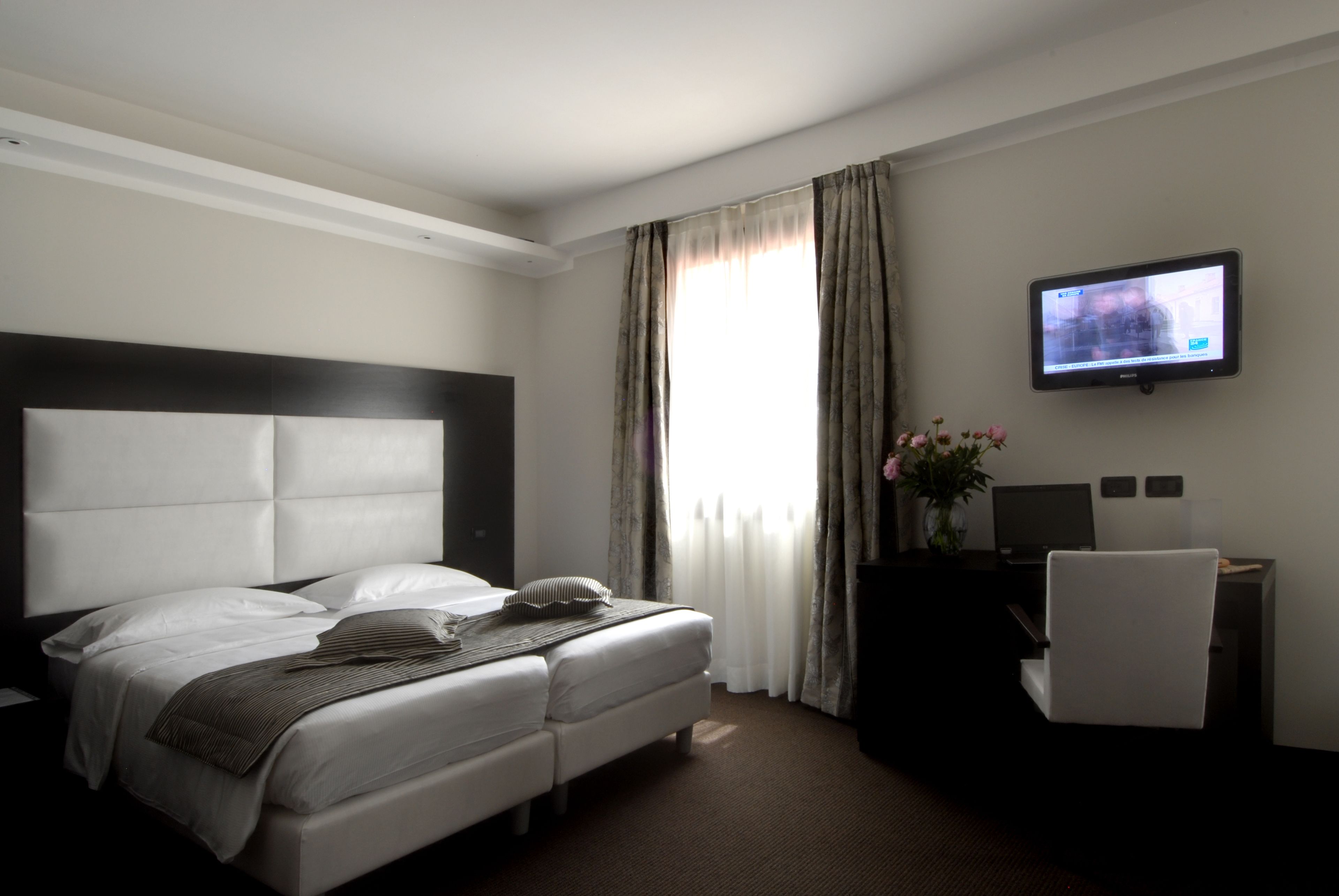 A hotel room with a bed, a desk, a chair, a television, and a window with curtains.