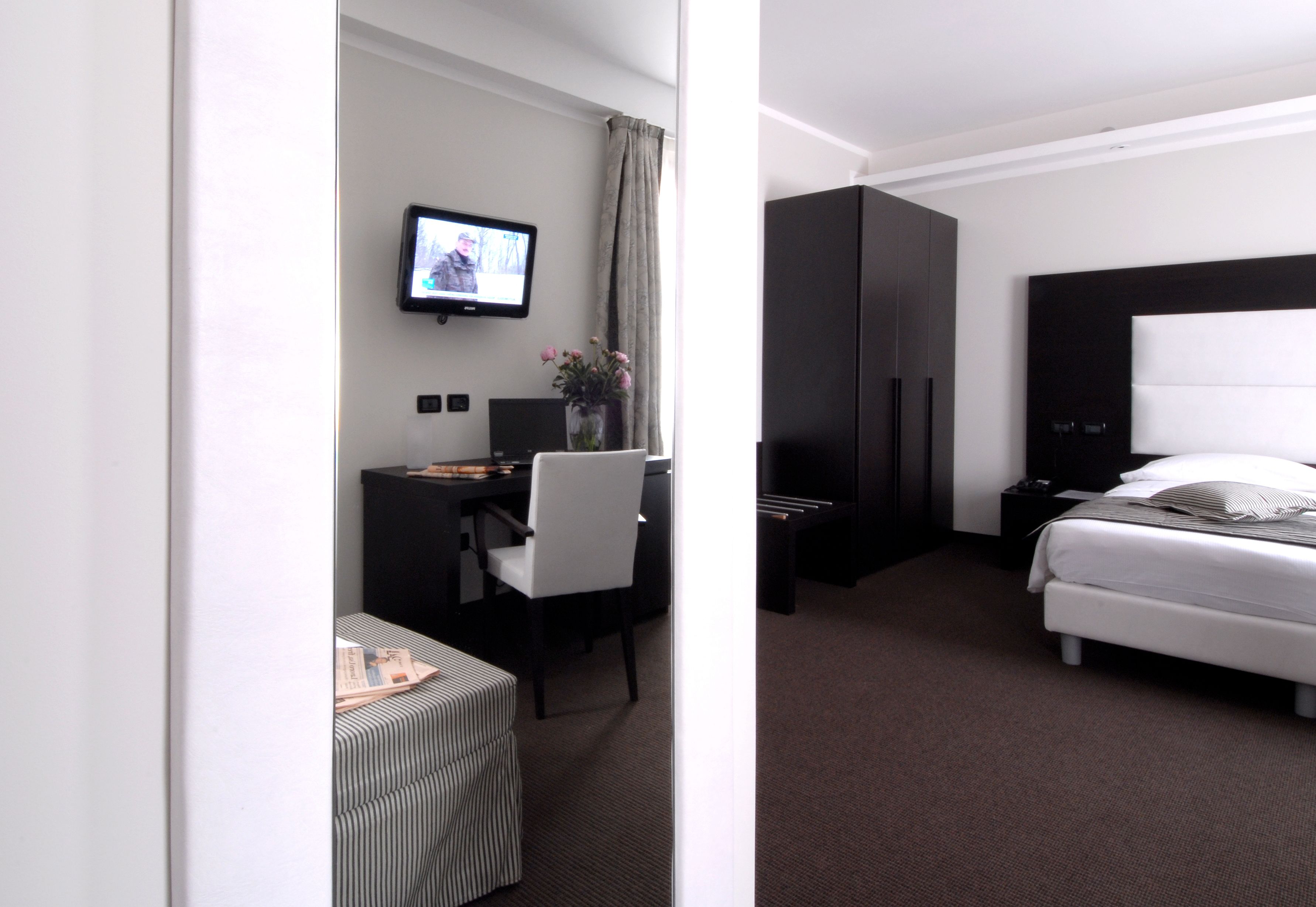 A hotel room with a bed, a desk with a chair, a television, and a wardrobe.