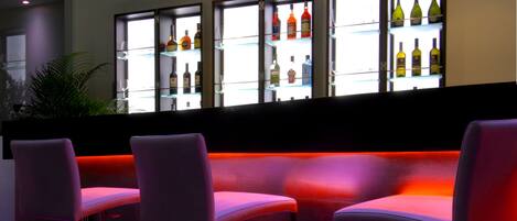 A bar area with a curved seating arrangement, a glass display case with bottles, and a red-lit floor.