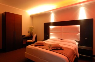 Una habitación de hotel con una cama grande, un escritorio con silla, un armario y un jarrón con flores.